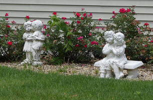 Two small sculptures of a little girl and boy in one he is standing, kissing her, with a gift behind his back. In the other they are seated, holding hands.
