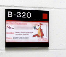 Name plate on classroom door giving teacher’s name, education, and degrees.