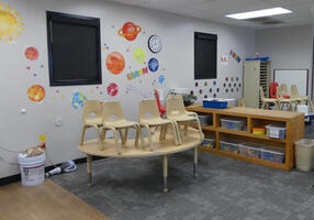 Childrens’ chairs on a table in child care area; planets painted on wall in background.