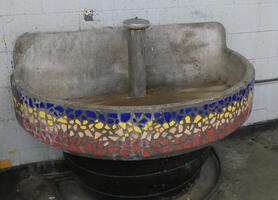 Water fountain/sink with multicolored ceramic mosaic chips on exterior.