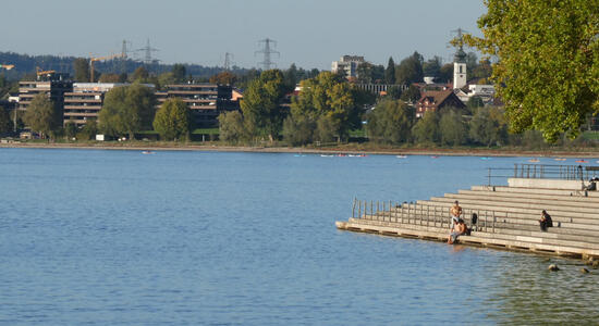 View of lake. At right, a staircase extending over the water where people are sitting and relaxing.