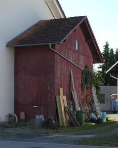 Large red-painted wooden shed with ladders and wood leaning up against it.