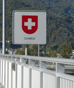 Sign on bridge. Red shield with white cross. Text: Schweiz (Switzerland)