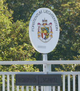 Oval sign with coat of arms and text Fürstentum Liechtenstein. Beneath the sign, a metal plate with Liechtenstein at left and Schweiz at right.