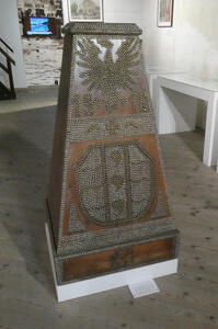 Trapezoidal wood box decorated with metal buttons that form shape of an eagle and the numbers 1918 above a coat of arms