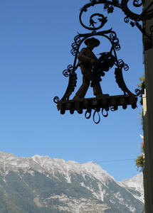 Metal sign with farmer carrying a large bunch of grapes. Mountain in background.