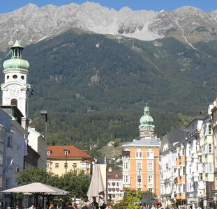 City scene. church at left foreground and right midground. Mountain back, forested up to near the top