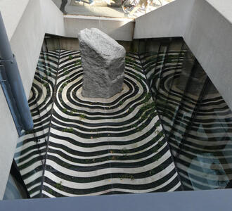 Large stone; at base, the floor is decorated in concentric rings in the shape of the stone.