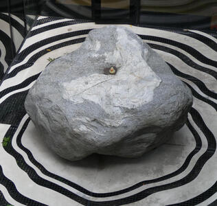 Stone on floor that has concentric rings in shape of stone painted on it. In middle of stone, an indentation with water and a rubber duck.