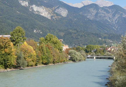 River in middle, trees with leaves changing colour at left, mountains in background.