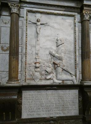 Relief carving of man with  sheathed sword at his side. He is on his knees praying to a crucifix